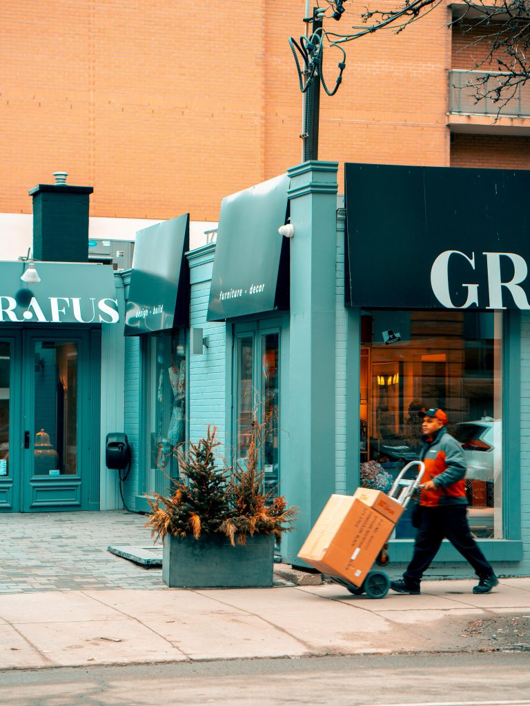 A delivery man walking past a green shop front.